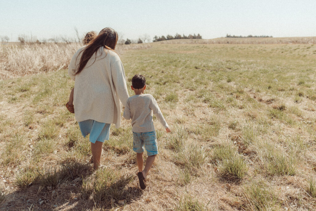 mother holds children while walking in a field during mother's day mini session in Lawton, OK