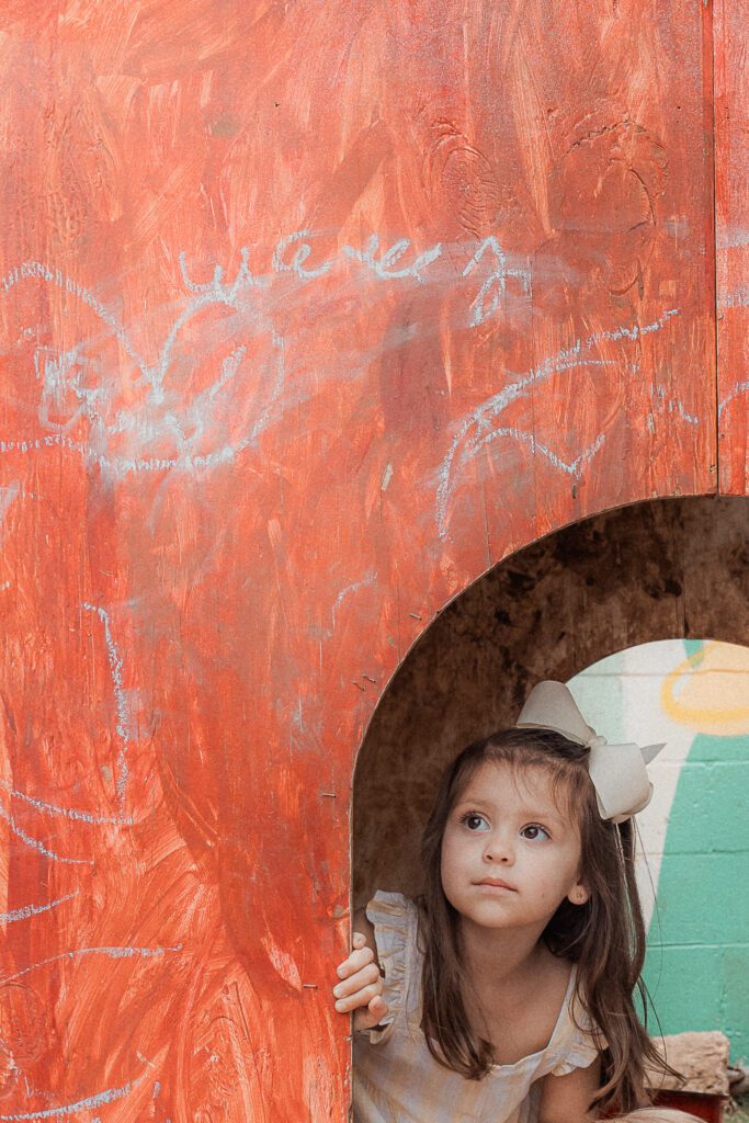 little girl peers out of play house at the scissortail school in lawton, ok